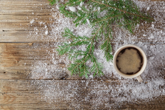 Tazza di tè e albero verde di natale su neve sulla tavola di legno