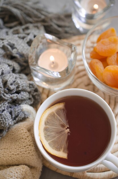 Tazza di tè e albicocche secche su un tavolo, candele e coperta a maglia.