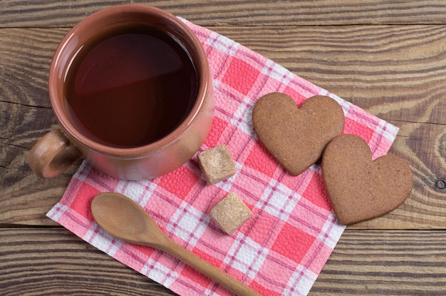 Tazza di tè e biscotti allo zenzero a forma di cuore sul tovagliolo rosso situato sulla vista dall'alto del tavolo di legno