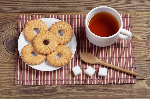 Tazza di tè e biscotti dolci nel piatto per la colazione su un tovagliolo di bambù sul tavolo di legno