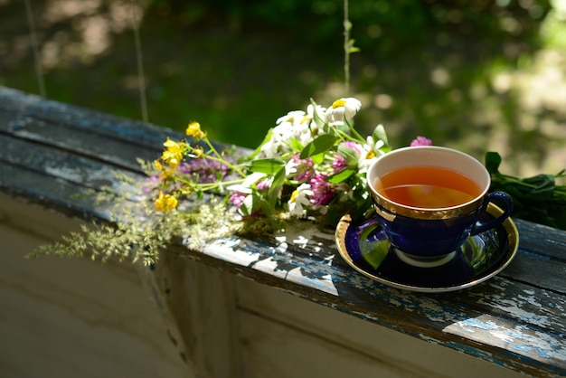 Tazza di tè e bouquet di fiori di camomilla fiori di campo su tavola di legno in giardino sfondo sfocato