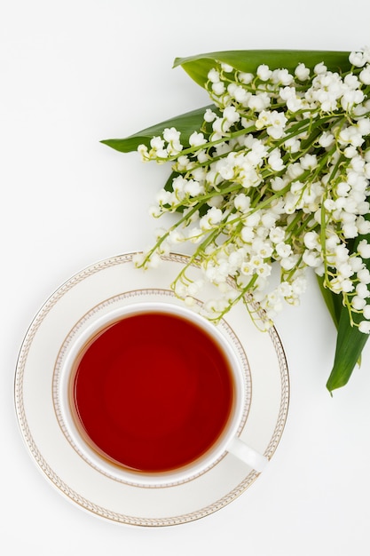 Tazza di tè e bouquet di mughetti su sfondo bianco Vista dall'alto