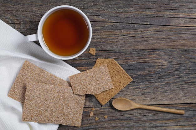 Tazza di tè e pane croccante intero e rotto per alimenti dietetici per colazione su un vecchio tavolo di legno, vista dall'alto. Copia spazio