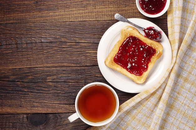 Tazza di tè e pane tostato con marmellata sulla tovaglia nascosta tavolo in legno. Vista dall'alto