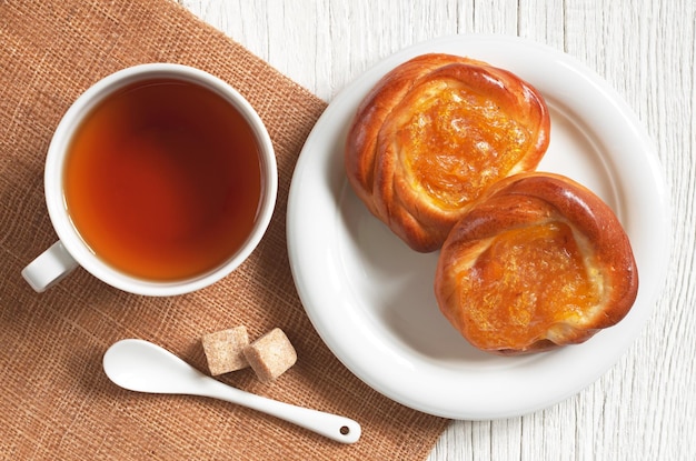 Tazza di tè e panini con marmellata di albicocche su tavola in legno rustico vista dall'alto