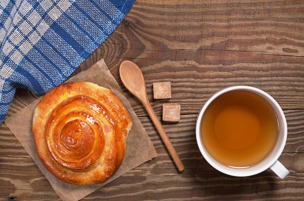 Tazza di tè e panino dolce per colazione sul vecchio tavolo in legno vista dall'alto