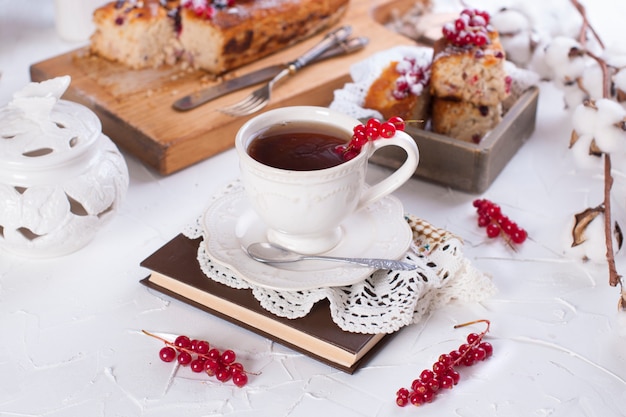 tazza di tè e piattino, cupcake con ribes rosso su tavola di legno e sfondo bianco, fiori di cotone