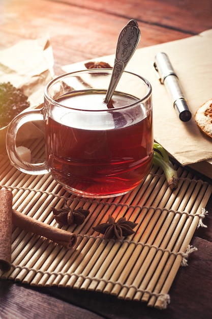 Tazza di tè, foglie di tè essiccate su carta Craft, busta di zucchero fette e penna su un tavolo di legno scuro