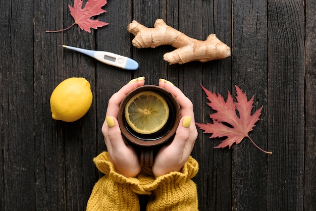 Tazza di tè in mani femminili con limone, zenzero e termometro