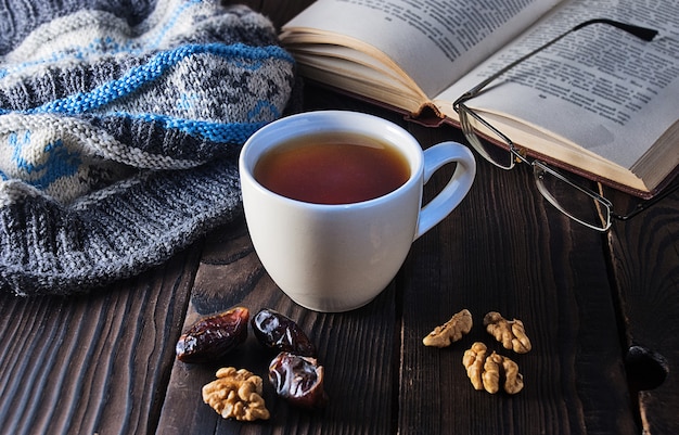 Tazza di tè, libro e berretto a maglia su un tavolo di legno