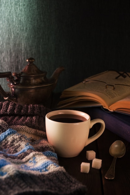 Tazza di tè, libro e berretto a maglia su un tavolo di legno