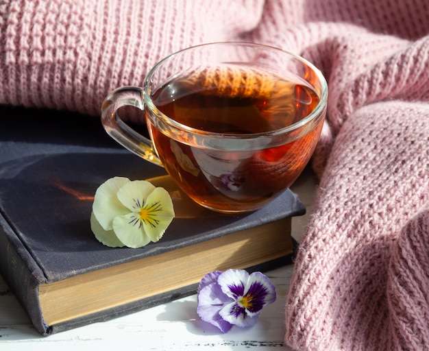 Tazza di tè, libro e fiori sul tavolo di legno chiaro. Concetto di lettura.