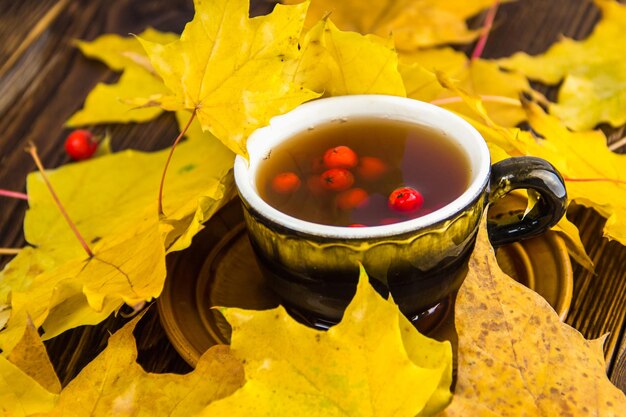 Tazza di tè marrone decorata con foglie di frassino e bacche rosse