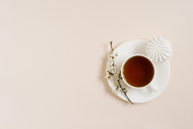 Tazza di tè nero con marshmallow e fiori primaverili di melo su sfondo beige
