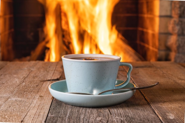 Tazza di tè o caffè prima di un accogliente caminetto, in una casa di campagna, vacanze autunnali o invernali, orizzontale.