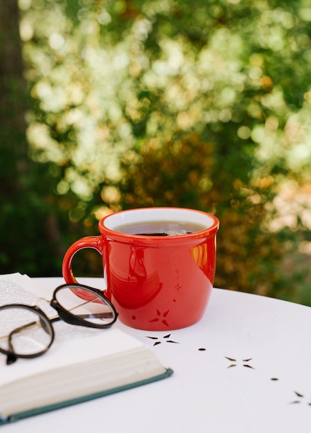 Tazza di tè rossa sul tavolo accanto a un libro e bicchieri in previsione dell'autunno