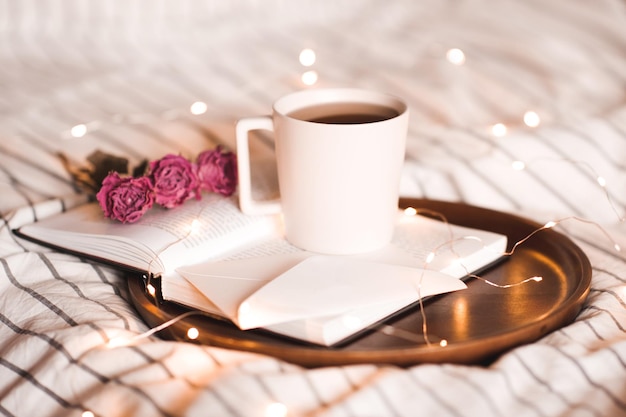 Tazza di tè sul libro aperto con fiori su luci in background. San Valentino. Buon giorno.