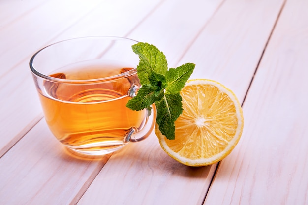 Tazza di tè, teiera di vetro, menta e limone su un tavolo di legno