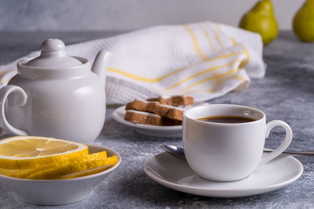 Tazza di tè, teiera, torte e limone su un tavolo