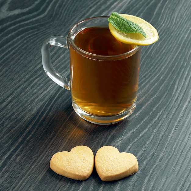 Tazza di tè trasparente con limone, menta e biscotti su un tavolo di legno. cibo da dessert