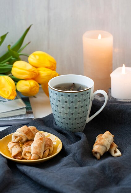 Tazza di tè, un piatto di biscotti, fiori di tulipano giallo e candele