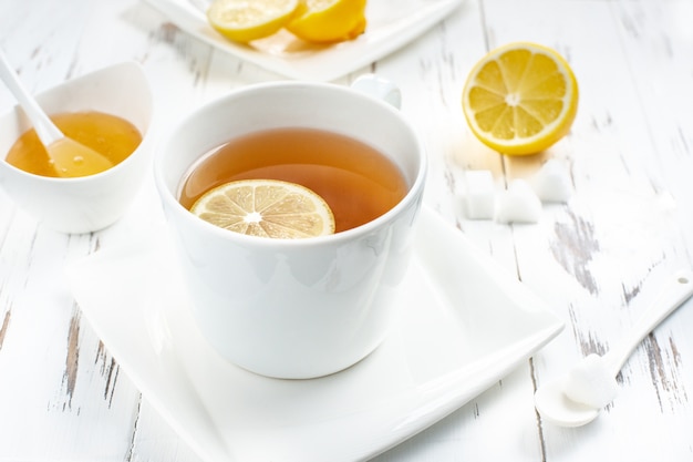 Tazza di tè verde con la fine del miele e del limone su sui precedenti di legno bianchi