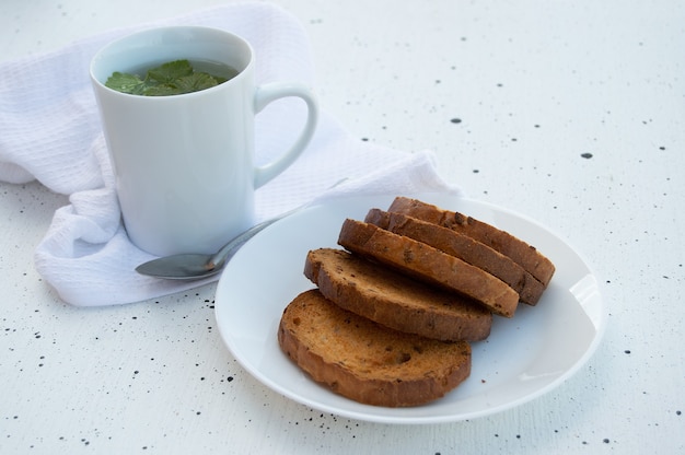 Tazza di tisana con foglie di ribes fresco e cracker dolci su un piatto su sfondo bianco