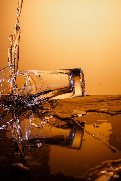 Tazza di vetro che esplode con acqua che si frantuma sulla superficie arancione