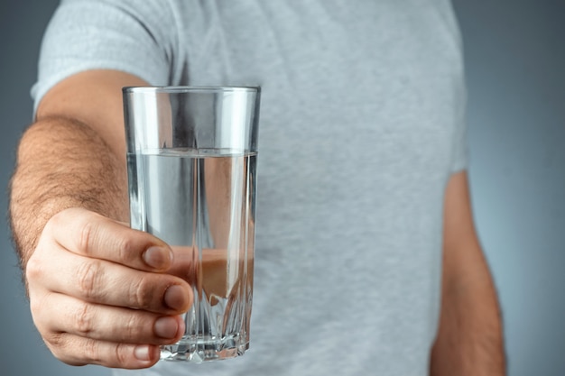 Tazza di vetro con acqua minerale pura in primo piano mani maschili su una superficie grigia. farmaci, trattamento, bevanda sana.