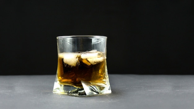 Tazza di vetro con whisky e ghiaccio su sfondo nero