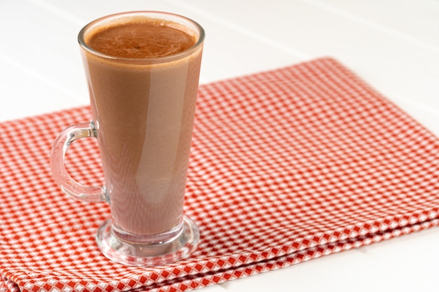 Tazza di vetro della bevanda di cacao sulla fine del tavolo in legno bianco su