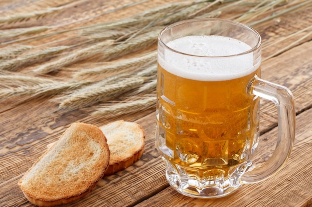 Tazza di vetro di birra e pane su tavole di legno con spighe d'orzo su uno sfondo.