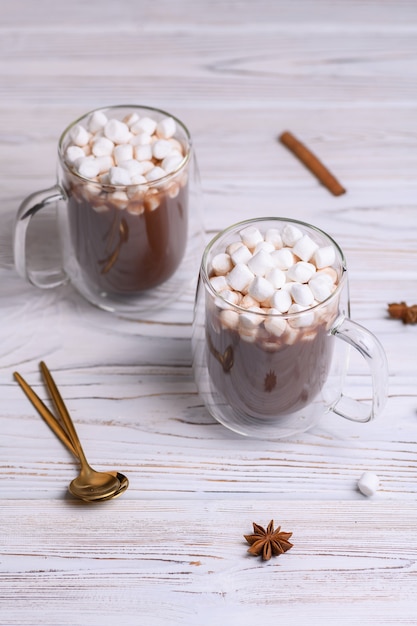 Tazza di vetro di cacao marrone con marshmeloy, su fondo di legno bianco.