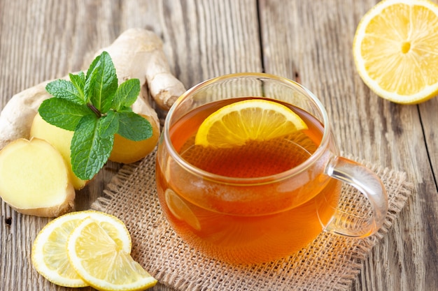 tazza di vetro di tè con limone, menta e zenzero sul tavolo in legno rustico.