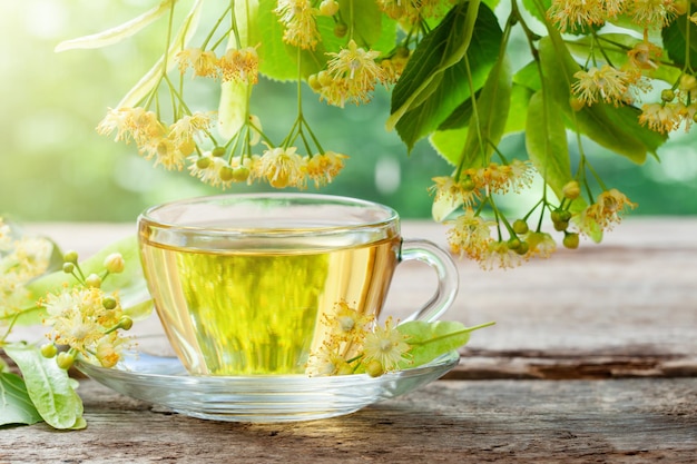 Tazza di vetro di tè sano con fiori di tiglio su tavola di legno fiori di tiglio Erboristeria