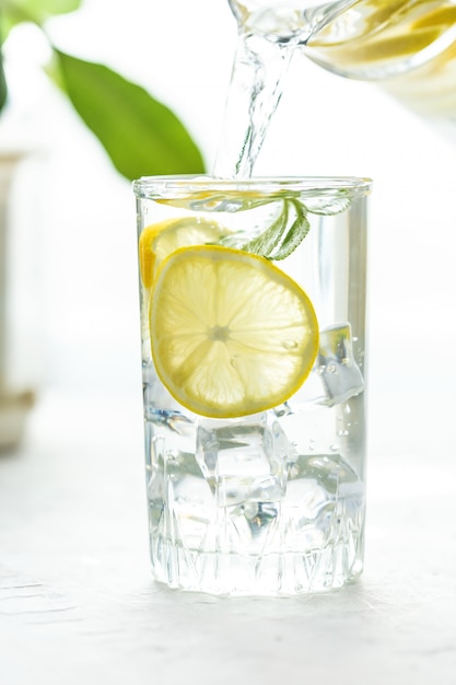 Tazza di vetro e una caraffa di acqua, ghiaccio, menta e limone su un tavolo bianco