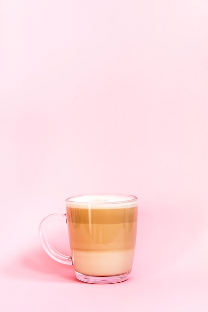 Tazza di vetro trasparente latte caldo caffè su uno sfondo rosa tenue.