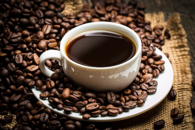 Tazza e fagioli di caffè su un fondo rustico. Caffè Espresso e un pezzo di torta con un ricciolo. Tazza di caffè e chicchi di caffè sulla tavola.