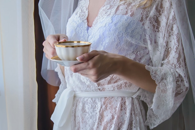 Tazza e piattino bianchi con tè nelle mani della sposa
