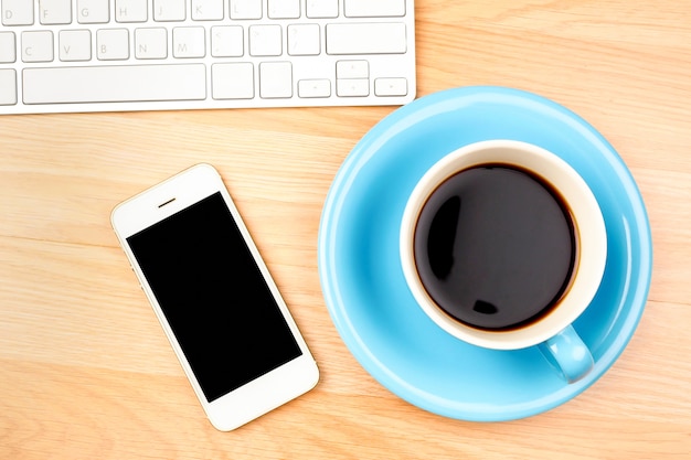 Tazza e smartphone di caffè blu e bianco con lo schermo in bianco sul fondo di legno della tavola.