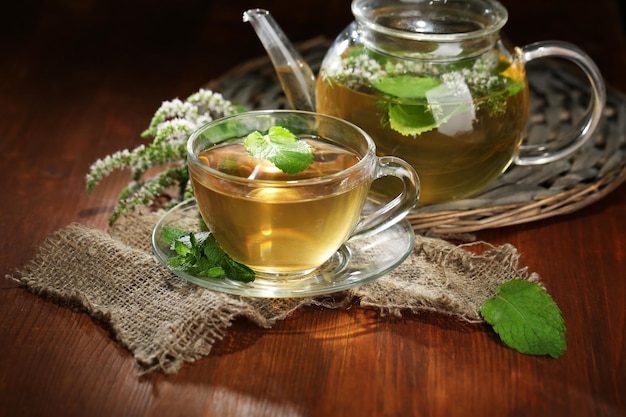 Tazza e teiera di tisana con fiori di menta fresca sulla tavola di legno