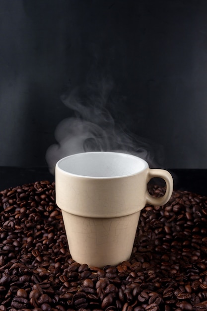 Tazza in ceramica di caffè nero caldo posto sul mucchio di semi di caffè su sfondo nero. caffè scuro caldo e vapore. avvicinamento.