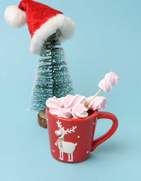 Tazza in ceramica rossa con cacao e marshmallow, dietro un albero di Natale