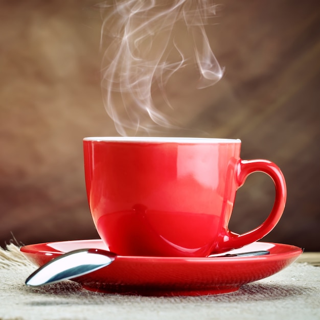 Tazza in ceramica rossa con caffè caldo su tavole di legno.
