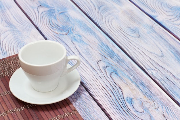 Tazza in porcellana bianca con piattino su tovagliolo di bambù con superficie in legno