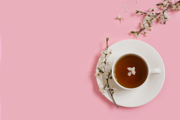 Tazza in porcellana bianca con tè nero. I rami di un melo in fiore giacciono su uno sfondo rosa delicato. concetto di primavera. Copia spazio. Lay piatto