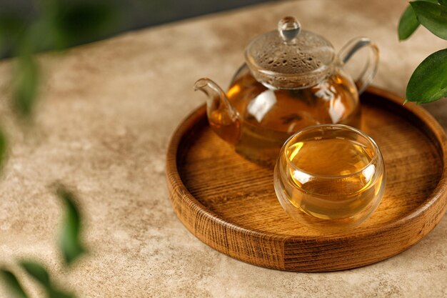 Tazza in vetro a doppia parete con teiera in vetro per tisane verdi su vassoio in legno e fondo beige