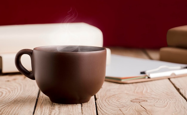 Tazza marrone con tè al cioccolato o caffè a vapore caldo libri su tavola in legno rustico con sfondo rosso