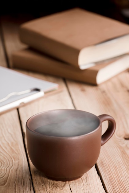 Tazza marrone con tè al cioccolato o caffè a vapore caldo libri su tavola in legno rustico