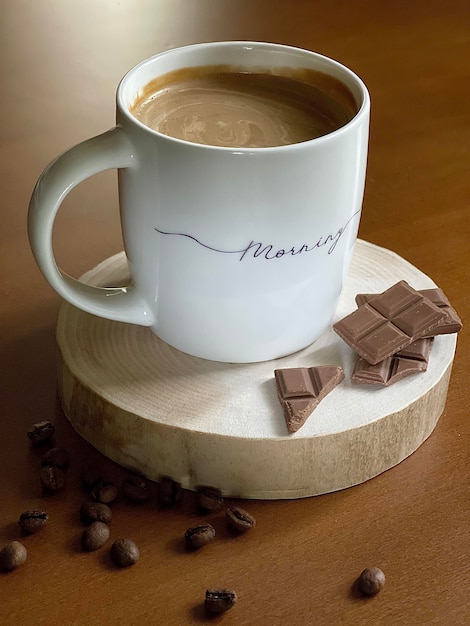 tazza mattutina di delizioso caffè con una barretta di cioccolato su uno sfondo di legno, chicchi di caffè